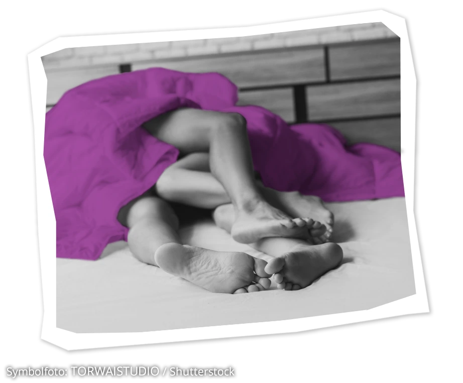 Beine und F&uuml;&szlig;e von zwei Menschen schauen unter einer Bettdecke hervor